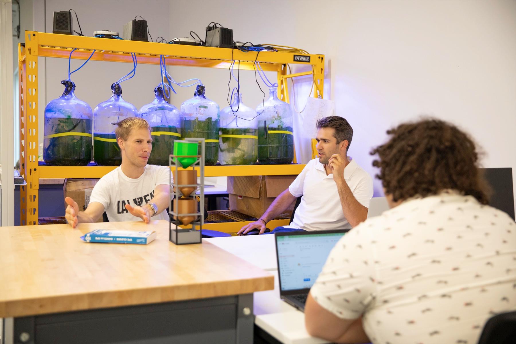 Clean Valley team members reviewing a prototype beside racks of algae cultures